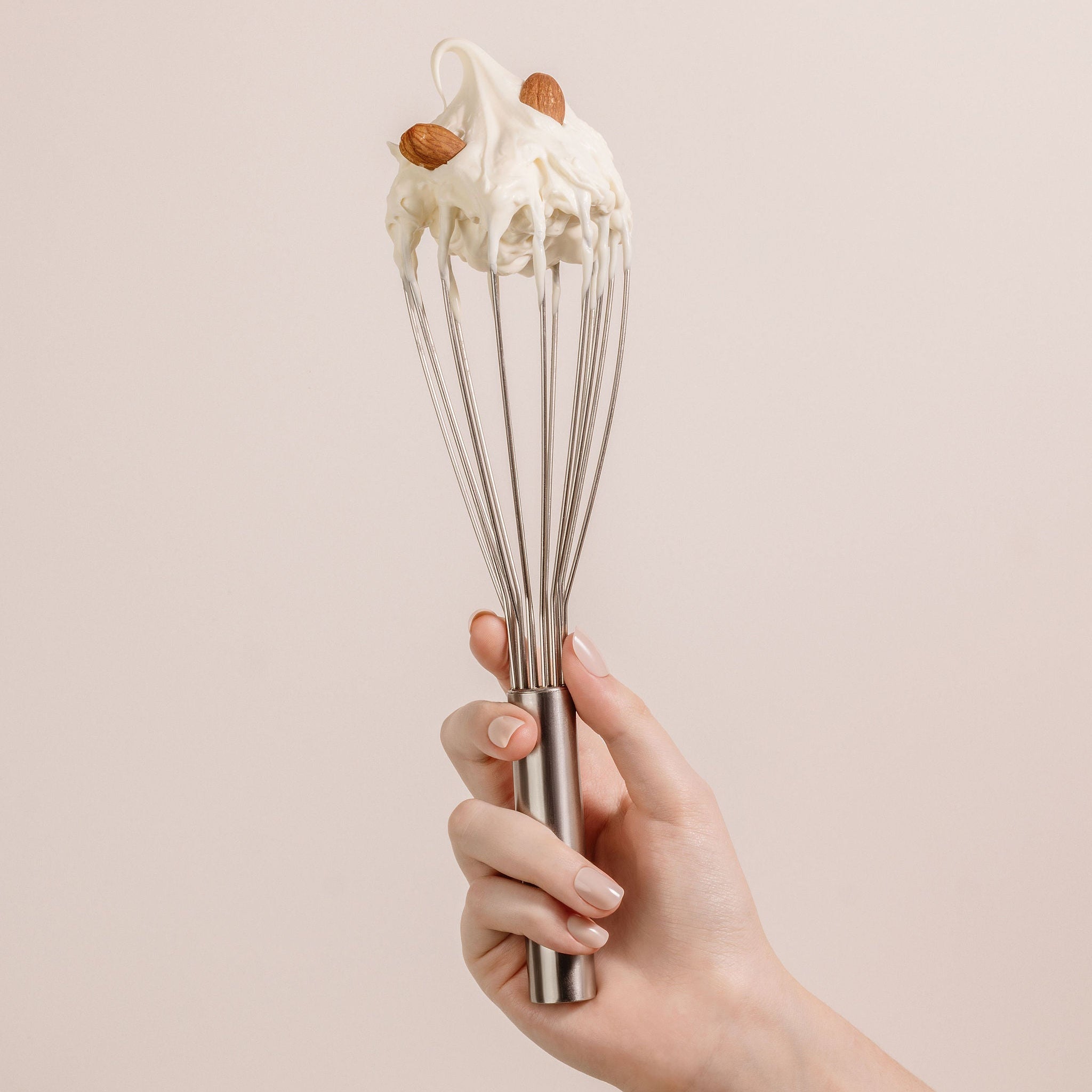 Nude nails hand holding a whisk with cream