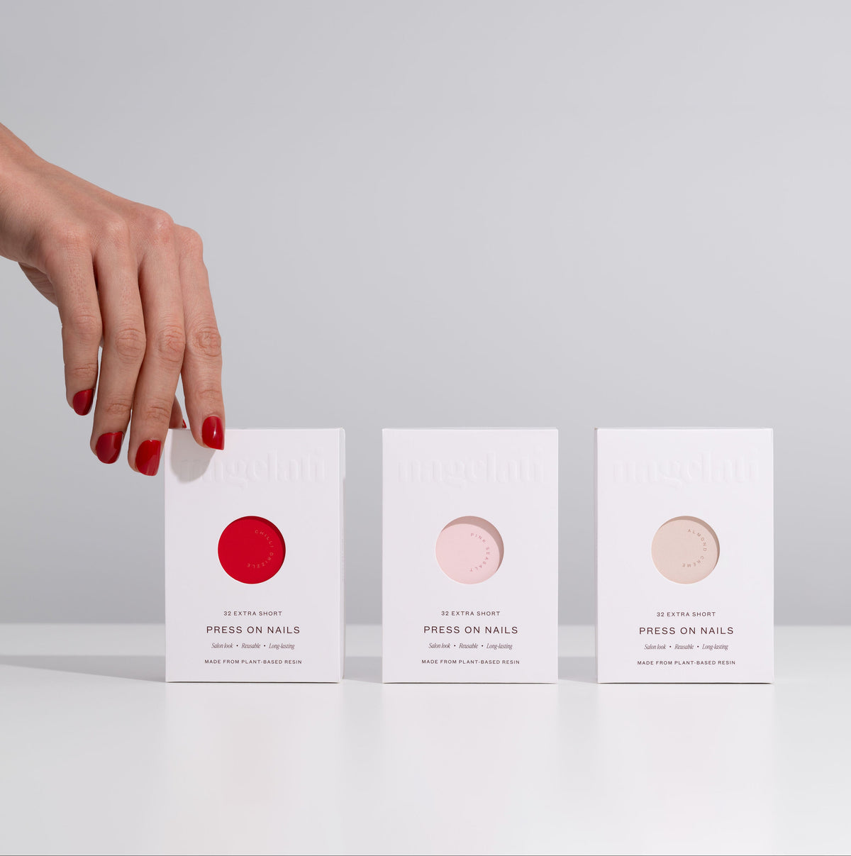Three boxes of press-on nails held by a hand with red nails